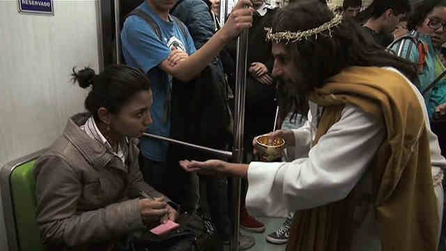 Mulher sentada conversa com ator vestido de Jesus no metro.