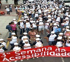 Na foto, participantes do evento andam pelas ruas. A comissão de frente carrega a faixa com o título da camapanha: 3ª Semana da Acessibilidade. Foto:Flávio Antunes/sn1