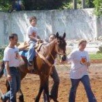 Menino anda a cavalo conduzido por um rapaz e uma moça