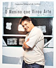 O artista Lucio Piantino posa em frente ao cartaz de sua exposição no STJ