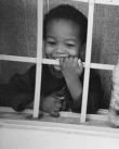 Foto de menino sorridente, atrás da grade de uma janela