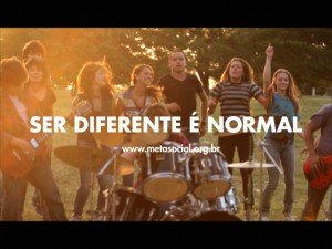 Moça tocando bateria em parque e jovens em volta, dançando. Inscrição Ser Diferente é Normal. www.metasocial.org.br.