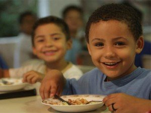 combate_fome Dois meninos sorridentes comendo, sentados a uma mesa