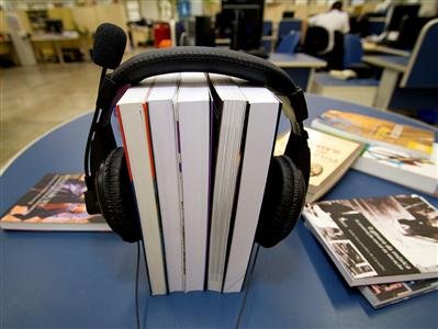 Livros em pe em cima de uma mesa com um fone em volta deles.