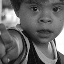Foto de menino em preto e branco, olhando e apontando para a câmera.