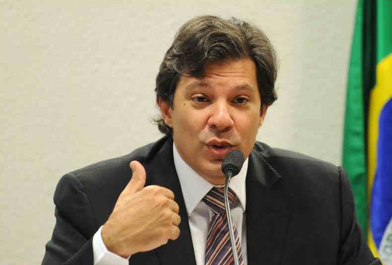 Ministro da Educação, Fernando Haddad, falando ao microfone com uma banderia do Brasil ao fundo