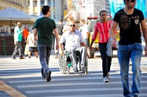 Homem em cadeira de rodas cruzando a faixa de pedestres em rua, entre outras pessoas. Homem em cadeira de rodas cruzando a faixa de pedestres em rua, entre outras pessoas.