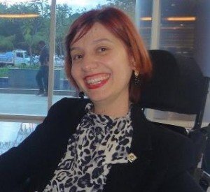 Ana Paula Crosara, vestindo blusa preta e branca e blazer preto, sorridente, com cabelos e batom vermelho.