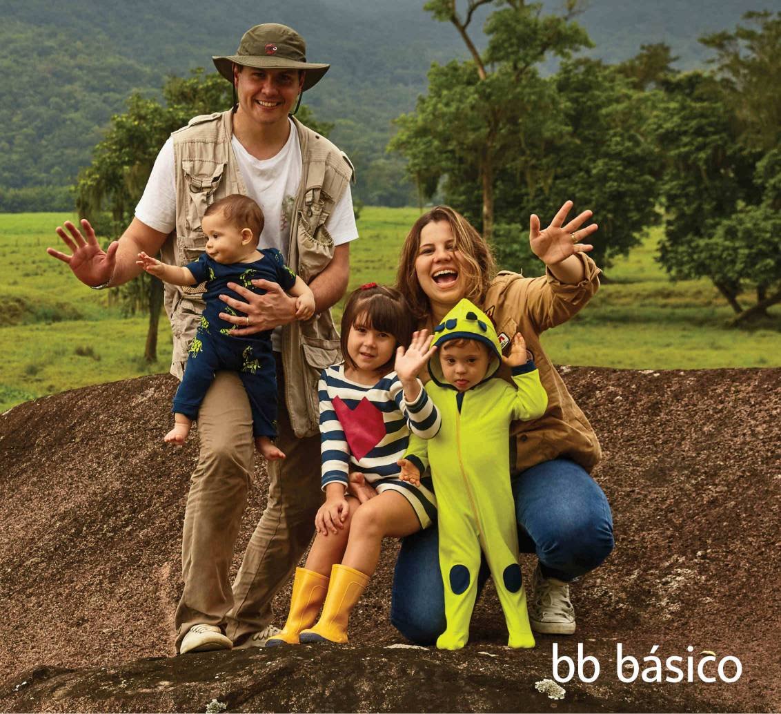 familia em cima de uma pedra, no campo. pai, homem com chapeu, com bebe no colo, apoiado no joelho, menina e menino com sindrome de down em frente a mulher, todos sorriem e dao tchau.