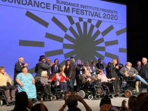 grupo de pessoas, várias em cadeira de rodas, no palco do festival de cinema Sundance 2020.