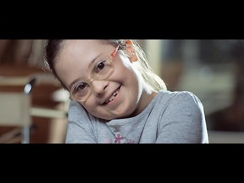 menina com sindrome de down de oculos sorri para a camera.