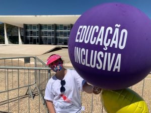 menina segura balao roxo em frente ao supremo escrito educacao inclusiva. ela esta de mascara.