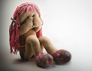 Boneca de pano sentada com mãos tapando o rosto.