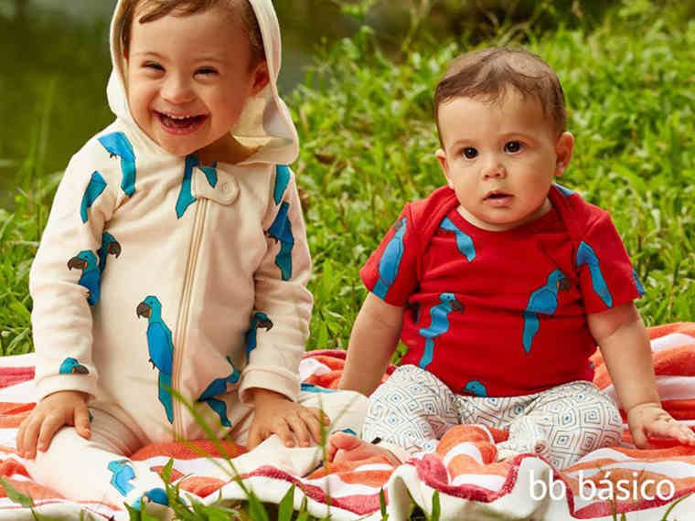 dois bebes sentados em cobertor em cima da grama. um deles tem sindrome de down.