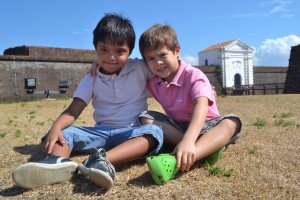 Dois meninos, um com síndrome de Down, outro sem, sentados no chão, cada um com a mão no ombro do outro.