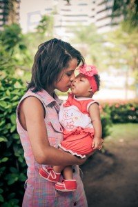 Mother kisses baby girl with microcephaly while holds her in her arms.