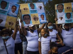 pessoas com camiseta branca com a inscrição just breath (apenas respire) em manifestação com cartazes com a foto do adolescente morto. alguns usam máscara.