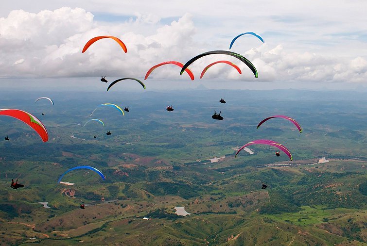 varios paraquedas coloridos voando no ceu e um campo verde abaixo.