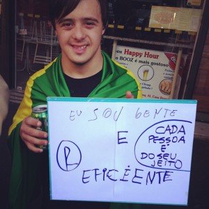 Jovem com síndrome de Down com cartaz "Eu sou gente e eficiente. Cada pessoa do seu jeito". 