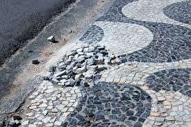 Calçada de pedras portuguesas com buraco e pedras soltas.