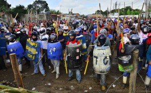 Diversos populares armados com paus, vestindo capacetes de moto e coletes improvisados com toneis de agua de plastico..