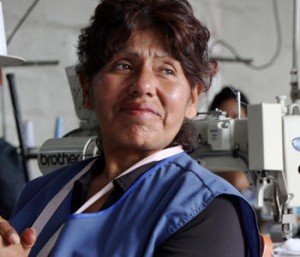 Mulher trabalhando em fábrica, sorrindo levemente.