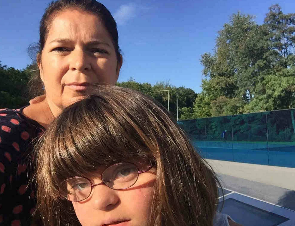 mulher. e menina em parque com vidro azul horizontal ao fundo.