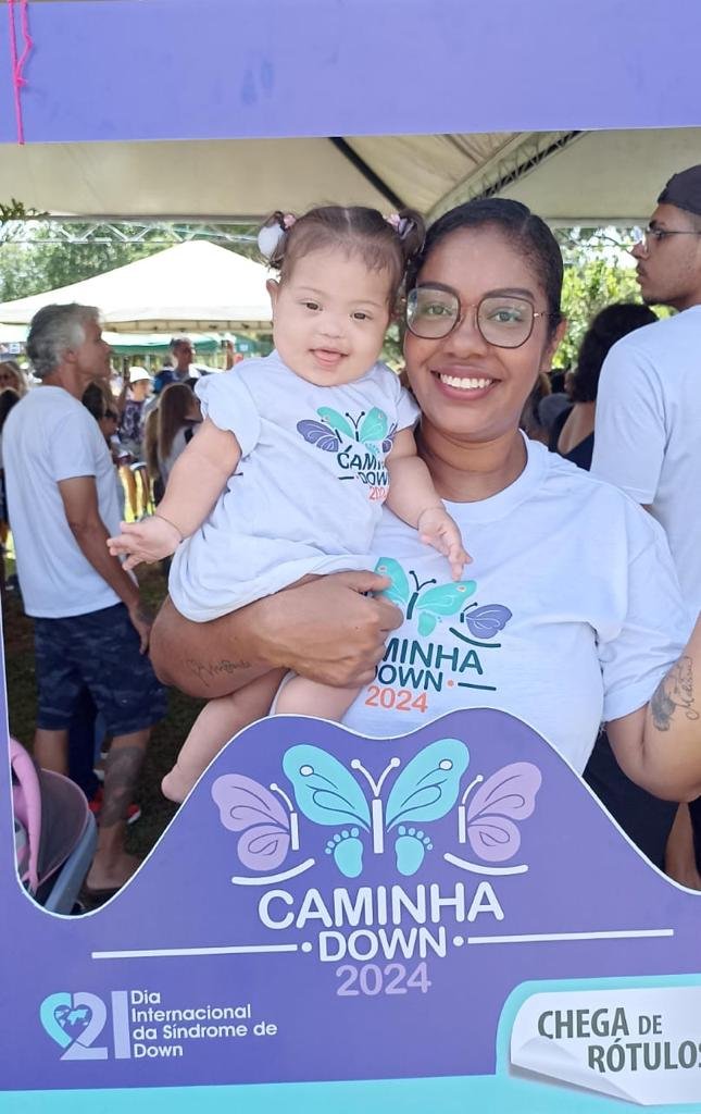 mulher segura bebe no colo, ambas com camiseta da caminhadown posando num quadro da caminhada.