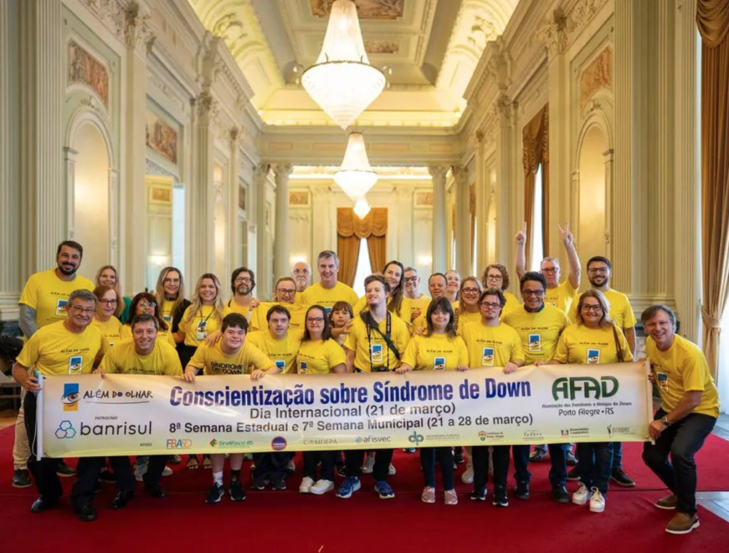 jovens de camiseta marela seguran faixa em salão da assembleia legislativa do rio grande do sul escrito conscientização sobre síndrome de down - afad.
