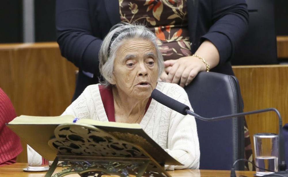 senhora falando ao microfone em mesa.