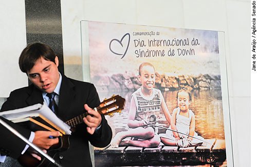 rapaz tocando cavaquinho. ao fundo, cartaz do dia internacional.