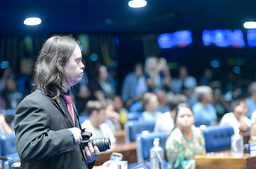 rapaz no plenario do senado, com câmera no pescoço.