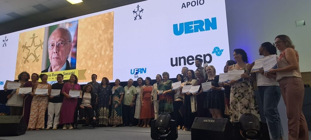 geral com todos que ganharam prêmio Romeu sassaki no auditório. foto de romeu no telão, apoio ufrn unesp.