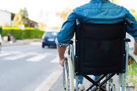 Pessoa cadeirante vista de costas na beira de uma rua e faixa de segurança.