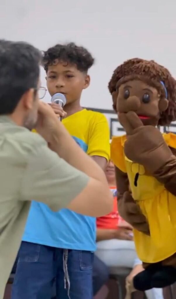 boneca cotinha, menino falando ao microfone e homem de costas.
