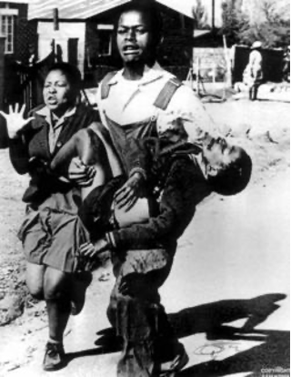 foto preto e branca de homem levando menino negro morto no colo, ao lado de mulher, ambos chorando.