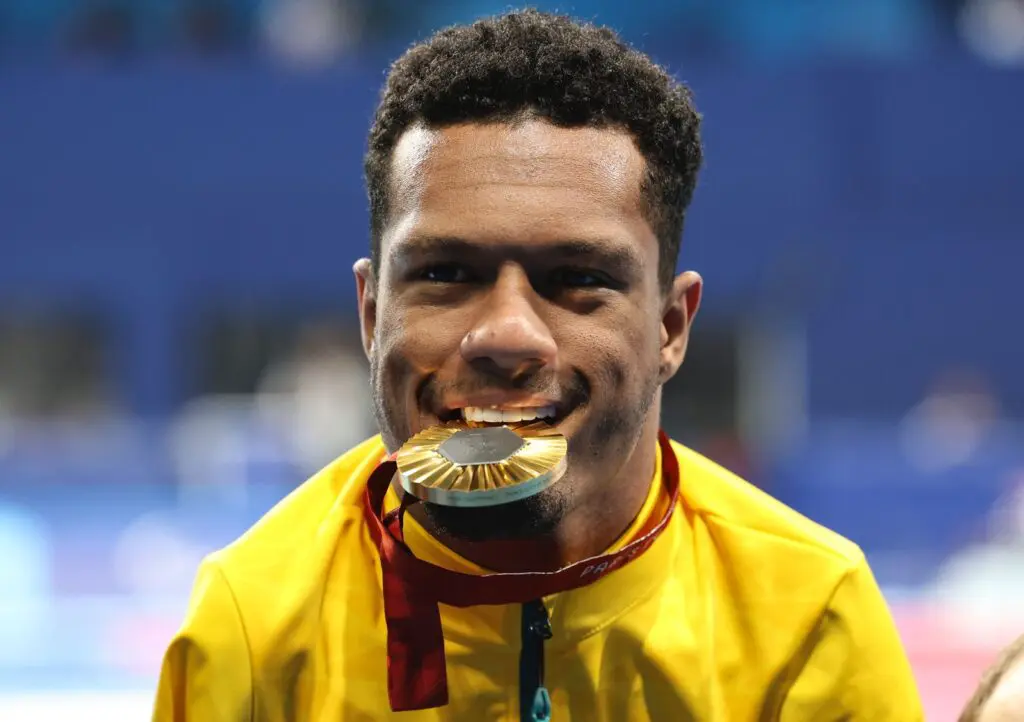 Gabriel Araújo posa para foto com medalha de ouro na boca em pódio em Paris 2024 | Foto: Alexandre Schneider / CPB