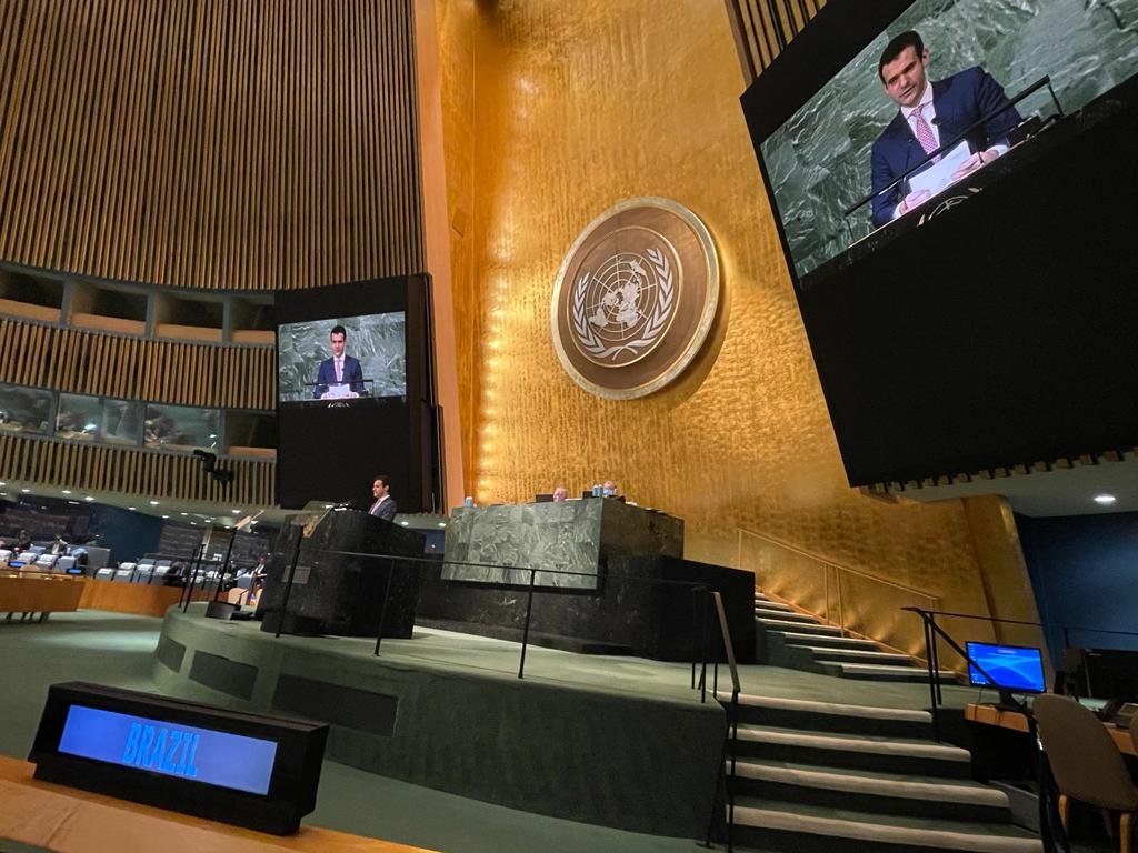 Plenário da ONU, diplomata aparece em duas telas projetadas lendo discurso. Em primeiro plano, placa digital escrito Brazil.