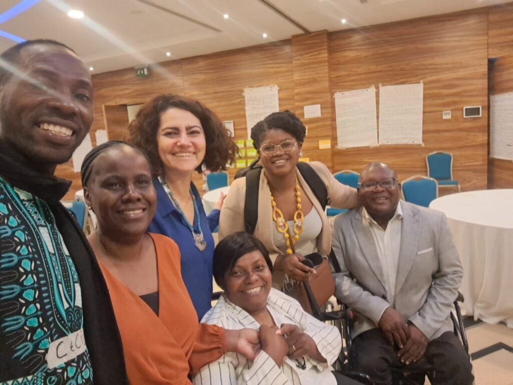 grupo de 4 mulheres, uma delas cega, e 2 homens, um deles em cadeira de rodas. todos sorriem.