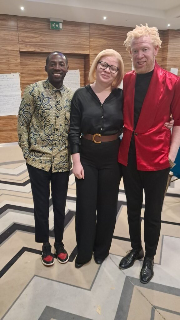 dois homens, um deles albino e uma mulher albino sorriem.