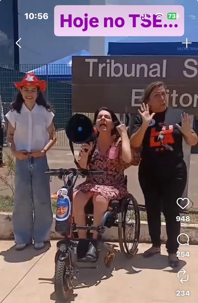 anna paula feminella com megafone ao lado de interprete de libra sna porta do tse.